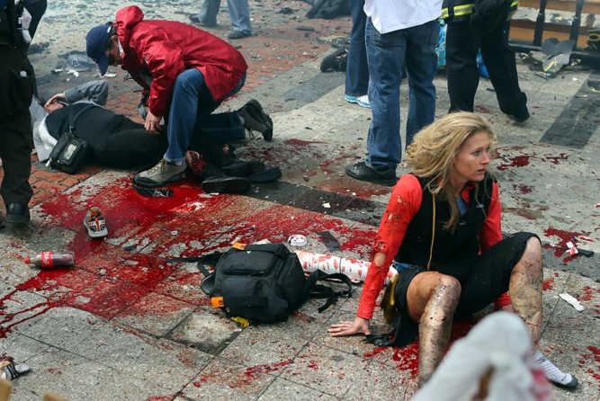Nicole Gross sits stunned on the Boylston Street sidewalk as Kevin Corcoran uses his belt as a tourniquet in an attempt to stem the bleeding of his wife Celeste's mangled legs. (Photo by John Tlumacki, December 15, 2013)