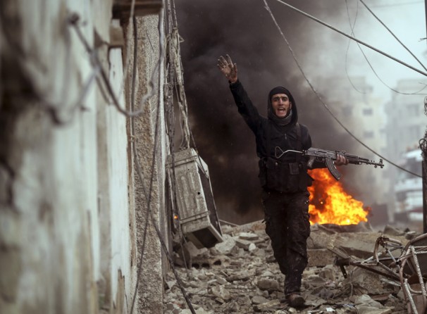 A Syrian rebel fighter gestures to comrades in front of a burning barricade as they attack an Army checkpoint the Ain Tarma neighborhood of Damascus. (January 30, 2013)