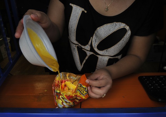 McAllen, Tex.: Adriana Gonzalez prepares one of the quick and cheap (and usually unhealthful) snacks that are pervasive in this part of Texas: melted cheese sauce poured over Cheetos. Hot Cheetos cost a dollar, and scores of drive-through convenience stores that accept food stamps offer it. In Hidalgo County, healthy food is more expensive, and many people can't get to the stores that sell it because they don't have cars. Meanwhile, the obesity rate nears 40 percent. (November 10, 2013)