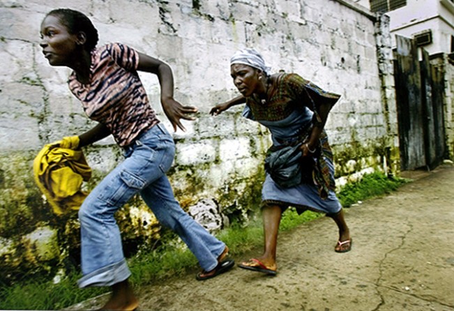 KEEPING LOW: Women run for cover on July 7th as the sound of heavy gunfire booms off of buildings and homes in downtown Monrovia where rebel and government soldiers fight for control. (Carolyn Cole)