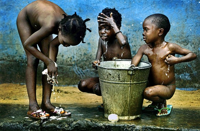 FEW COMFORTS: Ester Burges, 6, Sarrah Barbar, 7, and Sabay Ndebe, 5, bathe from a bucket of cold water at the Hannah B. Williams center. the number of orphans in war-devastated Liberia now tops 10,000, officials say. (Carolyn Cole)