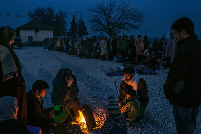 A refugee family from Syria gets warm around a bonfire as others line up to be registered in a reception camp, in Gevgelija, Macedonia (Mauricio Lima, The New York Times - November 21, 2015).