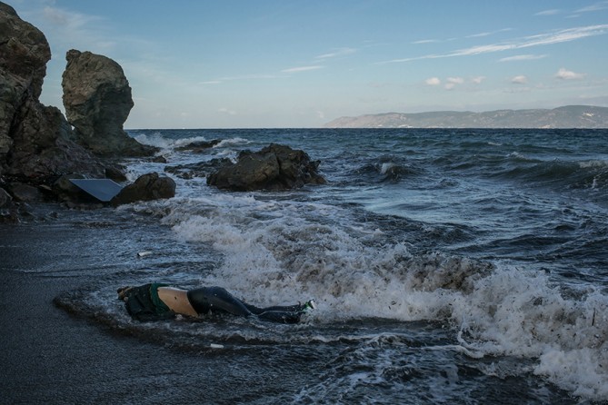 The body of a refugee who attempted to cross the Aegean Sea from Turkey, in the background, on the Greek island of Lesbos. Three other bodies, of a 12-year-old girl, a middle-age man and an elderly man, were also found that morning (Mauricio Lima, The New York Times - November 1, 2015). 