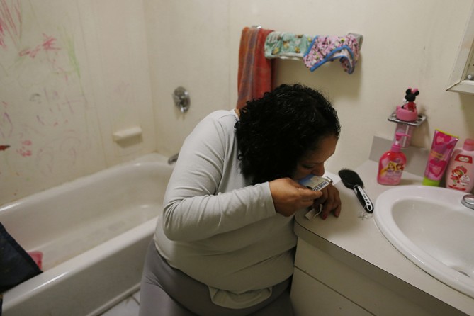 With the bathroom door locked to keep her daughters out, Raquel leans over and snorts heroin inside her apartment. Moments earlier, Estrella had tried to block her mother's way into the bathroom, and now the girls are crying outside of the door as she gets high (Jessica Rinaldi, The Boston Globe).