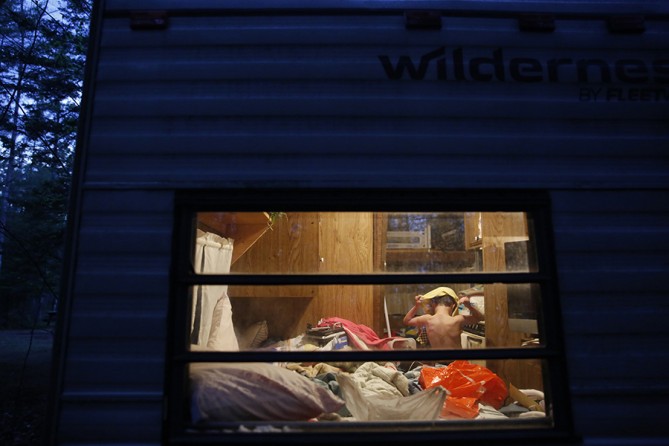 Strider pulls his pajamas over his head as he changes in his grandparents' bedroom inside the cramped camper. With nowhere else to go, the Grants told the boys they were going camping and the family of four squeezed into the 24-foot camper with their cat and two dogs (Jessica Rinaldi, The Boston Globe).