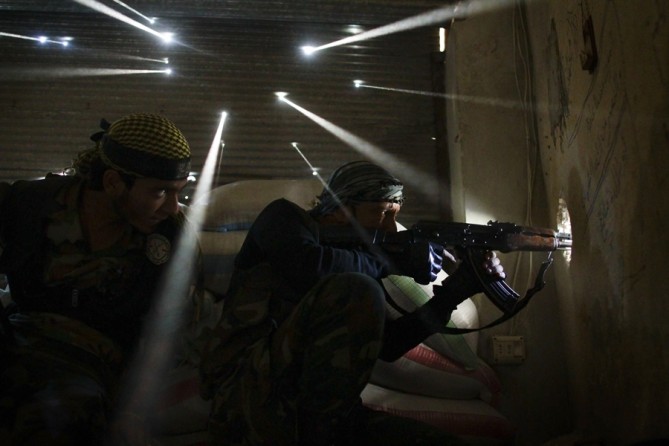 Two rebel soldiers in Syria guard their position in the Karmel Jabl neighborhood of Aleppo as light streams through more than a dozen holes made by bullets and shrapnel in the tin wall behind them. The dust from more than one hundred days of shelling, bombing and firefights hung in the air. Karmel Jabl is strategically important because of its proximity to the main road that separates several of the main battlegrounds in the city. (Photo taken October 18, 2012)
