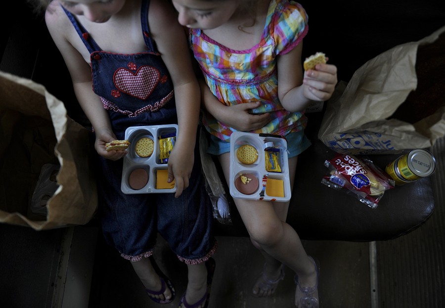 Greenville, Tenn.: Six-year-old Hannah Knight, left, and Kaylee Arwood, 4, eat Lunchables as part of their meal. Apple slices, fruit cups and low-fat chocolate milk also were offered. Scores of poor children are served lunch each weekday during the summer as the Lunch Express bus visits trailer parks and housing projects. (July 7, 2013)