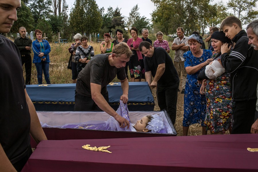 Sept. 8, 2014. A cemetery employee covers the body of 6-year-old Karolina Baykina as another closes the coffin of her brother, 10-year-old Nikita, in the small village of Lebedinskoye. Their injured grandmother, Lyubov Baykina, 53, third from right, is comforted. The two children died during shelling. (Mauricio Lima for The New York Times)