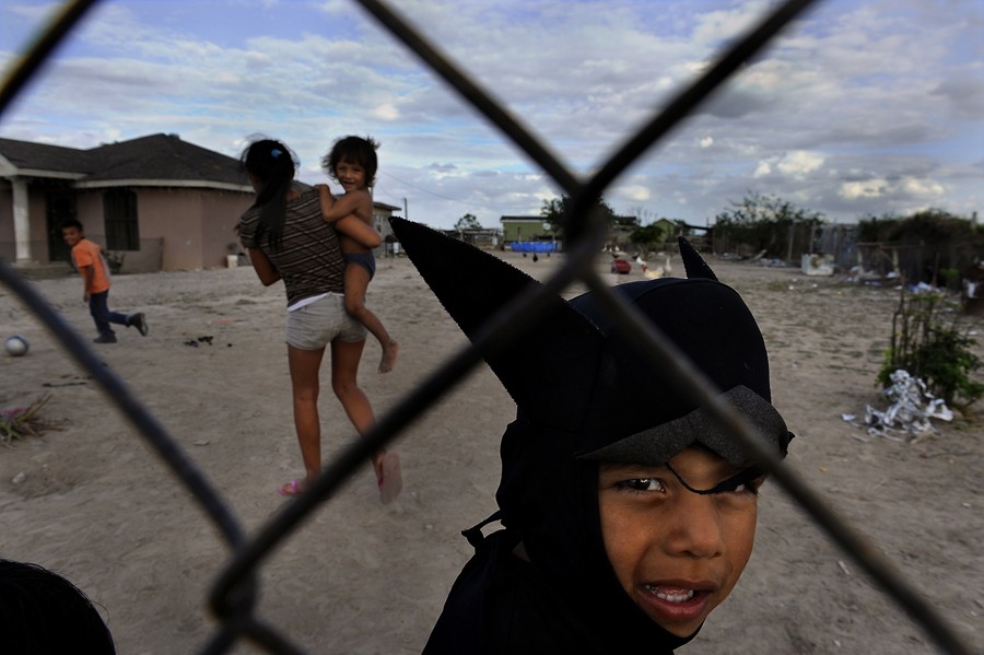 Alamo, Tex.: Jeremy Castro, 4, in his Batman costume, peers through a fence at his home. At far left is his brother Pablo, 6; at center is his sister, Emily, 13, holding brother Jaime, 2. They live in Hidalgo County, Tex., one the poorest and fastest-growing counties in the United States, and one where obesity is a growing problem. The USDA's response is an education program that teaches families on food stamps how to stretch their benefits and choose more healthful foods. Emily says she participated in the