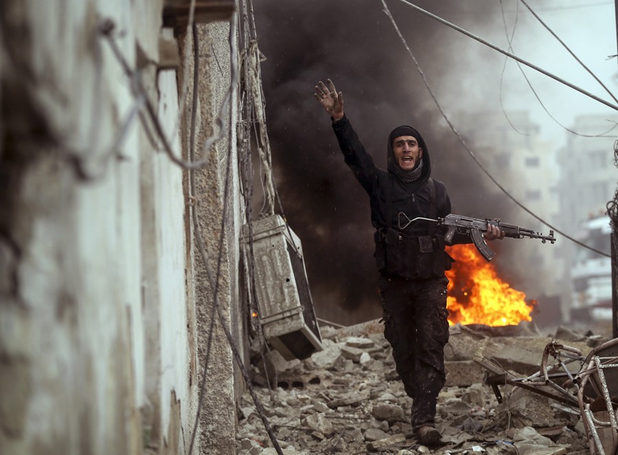 A Syrian rebel fighter gestures to comrades in front of a burning barricade as they attack an Army checkpoint the Ain Tarma neighborhood of Damascus. (January 30, 2013)