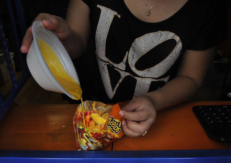 McAllen, Tex.: Adriana Gonzalez prepares one of the quick and cheap (and usually unhealthful) snacks that are pervasive in this part of Texas: melted cheese sauce poured over Cheetos. Hot Cheetos cost a dollar, and scores of drive-through convenience stores that accept food stamps offer it. In Hidalgo County, healthy food is more expensive, and many people can't get to the stores that sell it because they don't have cars. Meanwhile, the obesity rate nears 40 percent. (November 10, 2013)