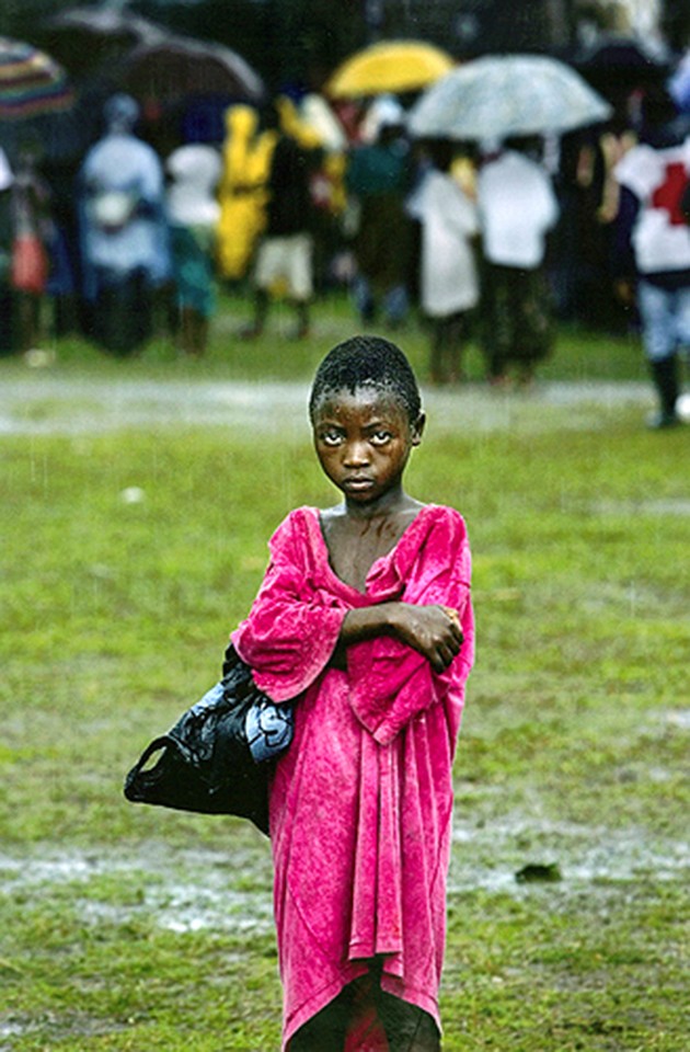 AMID THE TRHONG: Patirnel Boima stands in the center of a rain-drenched stadium field where more than 30,000 people have taken refuge. Rebels have been at war with President Charles Taylor, a former warlord, since 1989. (Carolyn Cole)