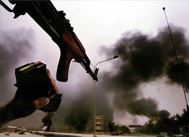 Surrounded by the smoke of destroyed Iraqi miliary equipment, Air Force Lt. John Blocher -- assigned to the 3rd Brigade Combat Team -- saves ammunition by using a recovered Iraqi-issued AK-47. (David Leeson)