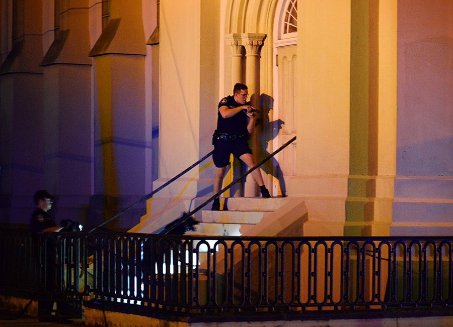 Charleston police officers search for a shooting suspect on the grounds of a church in downtown Charleston, S.C. A white man had opened fire during a prayer meeting inside nearby Emanuel AME Church killing nine people attending a Bible study. The shooting left behind devastated families and a shocked community. The shooter remained at large Thursday morning (Matthew Fortner, The Post and Courier - June 17, 2015).