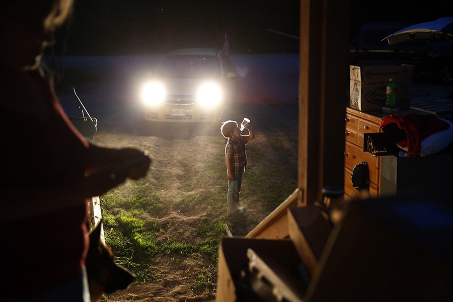 Gallagher cools off with a drink as Larry and Lanette scramble to pack by the light of their car headlights as the midnight eviction deadline inches closer. The landlord has cut the power and put locks on the electrical boxes in an attempt to force them off the property (Jessica Rinaldi, The Boston Globe).