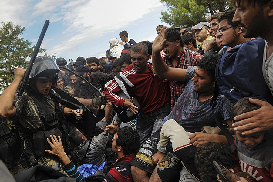 A Macedonian police officer raises his baton towards migrants to stop them from entering into Macedonia at Greece's border near the village of Idomeni, Greece (Alexandros Avramidis, Thomson Reuters - August 22, 2015).