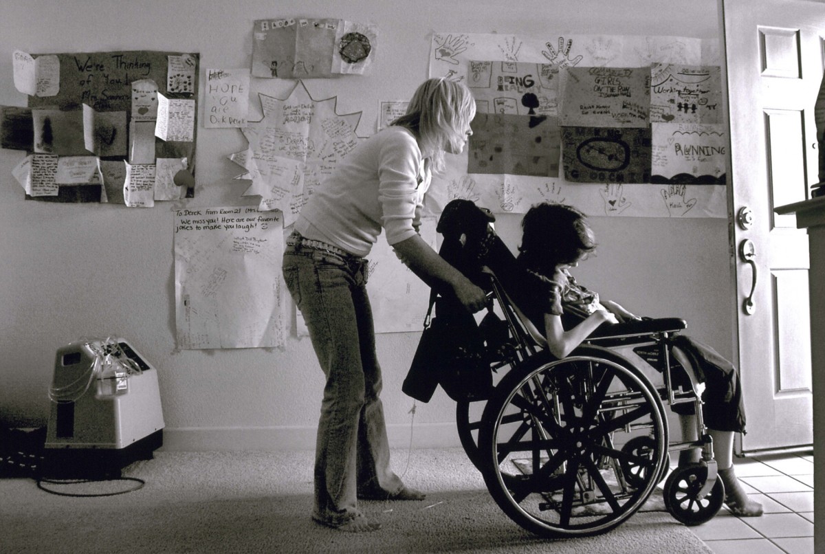 In an effort to get Derek outside, Cyndie wheels him through the front door passing by artwork and cards given to her son by classmates at Bridgeway Island Elementary School. "Just like a newborn, he needs to get out and get some air," she says. It was his last trip outdoors.