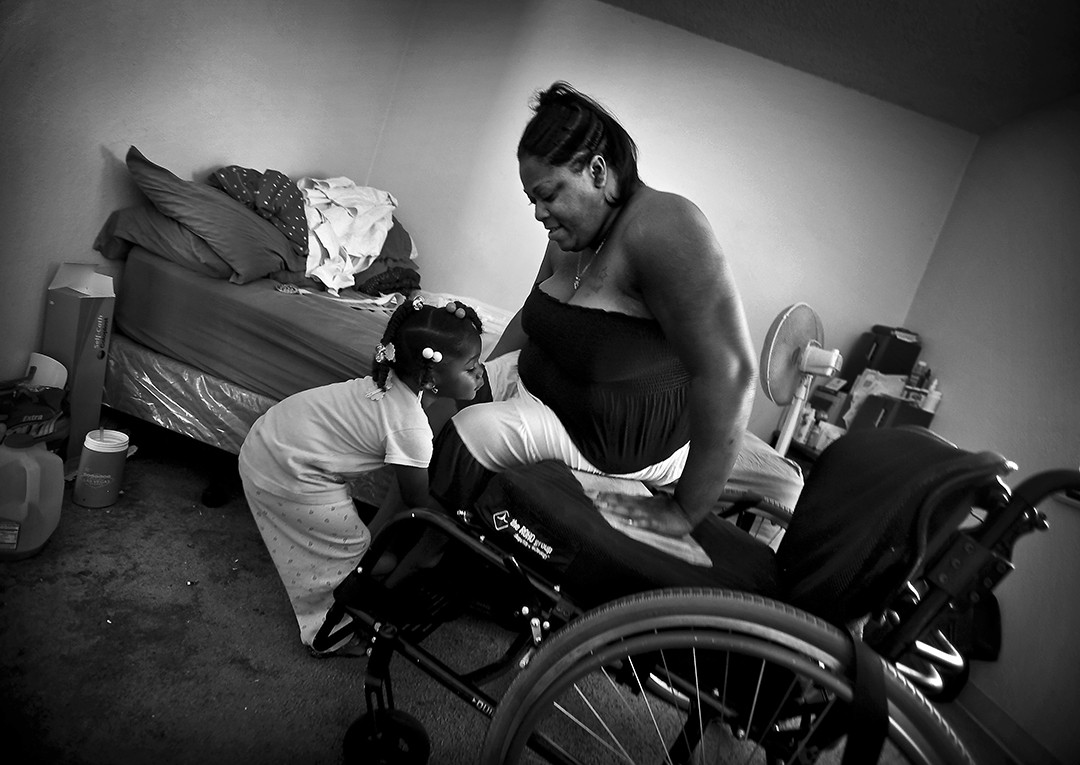 Rose Smith was coming home from the market to prepare for a Memorial Day potluck. She heard gunshots outside her apartment in Watts Nickerson Gardens housing project and ran. She was reaching for the front door when she felt the bullets tear into her arm, her jaw, and her back. She was three months pregnant. Both she and the baby survived, but Smith will never walk again. She named the baby Miracle.  In this photo, Miracle lifts her mother’s leg as Rose Smith slides into her wheelchair. The family had stem 